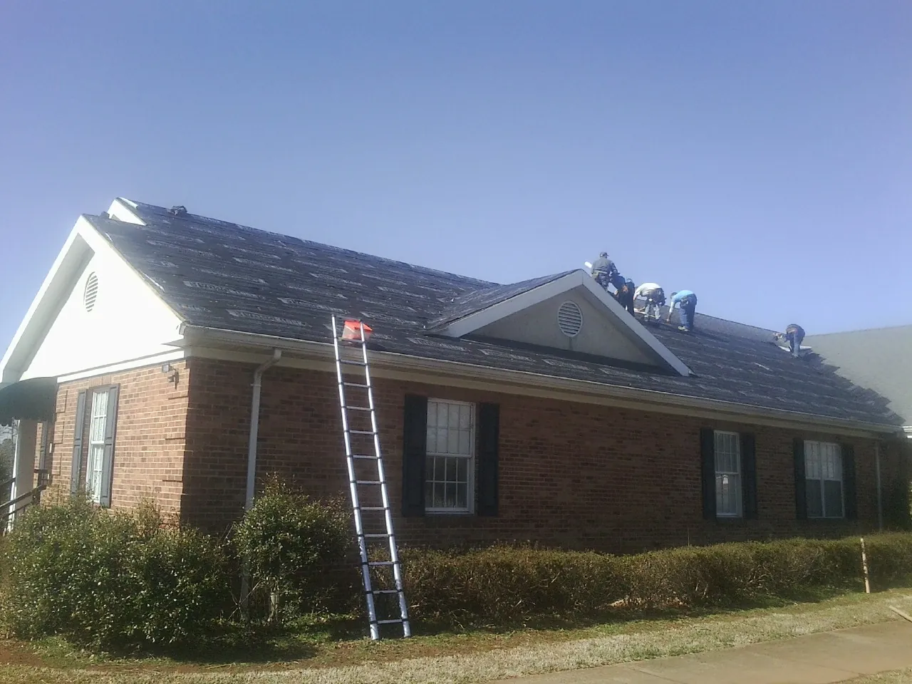Crew tearing shingles off a brick ranch roof with a ladder set — Metal Roof Repair work by our crew in Valley City
