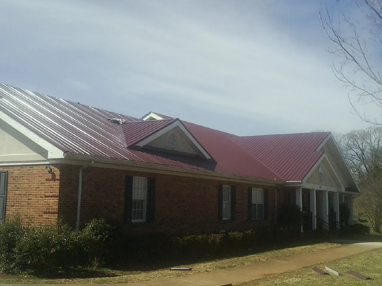 Red metal roof with gabled entries on a long brick building, from a Hail Damage Roof Repair job in Valley City