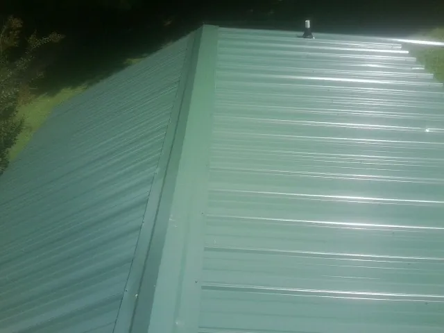 New green metal panels meeting at the ridge of a roof — Flat Roof Repair work by our crew in Valley City