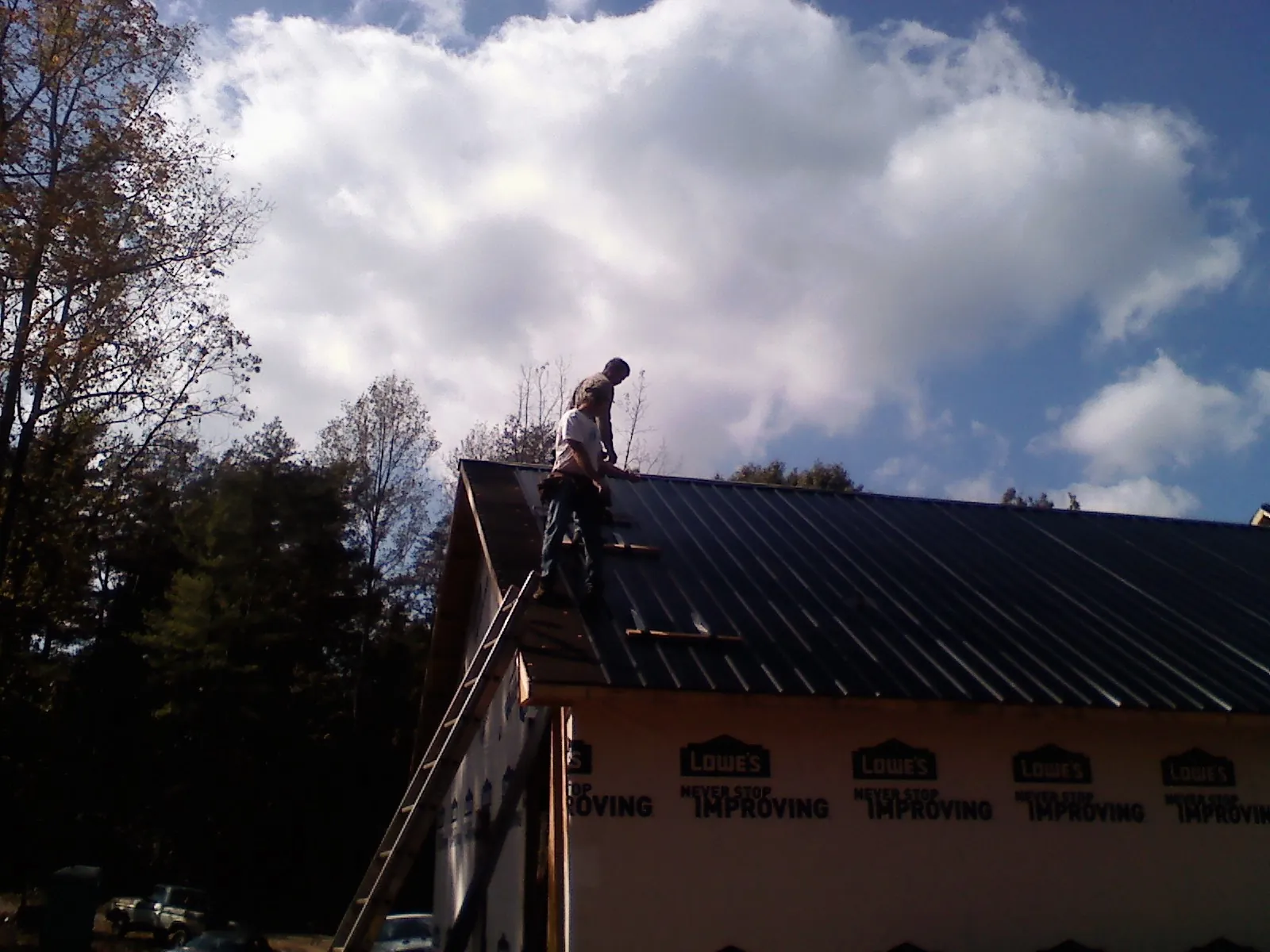 Roofer fastening dark metal panels high against a cloudy sky, from a Roof Inspection job in Valley City