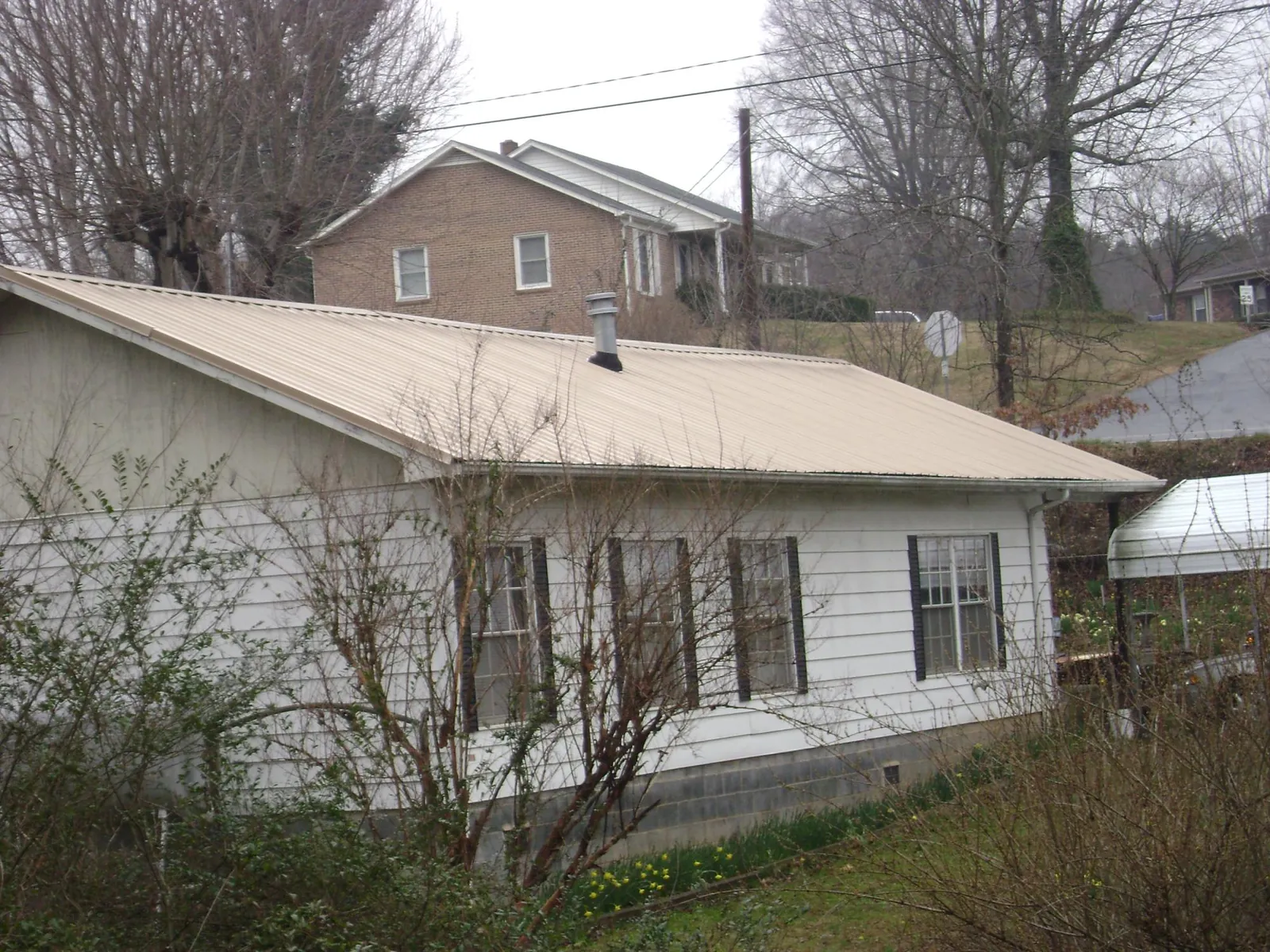 Tan metal roof on a white sided house set into a hillside — Commercial Roofing by Roofing Brothers in Valley City